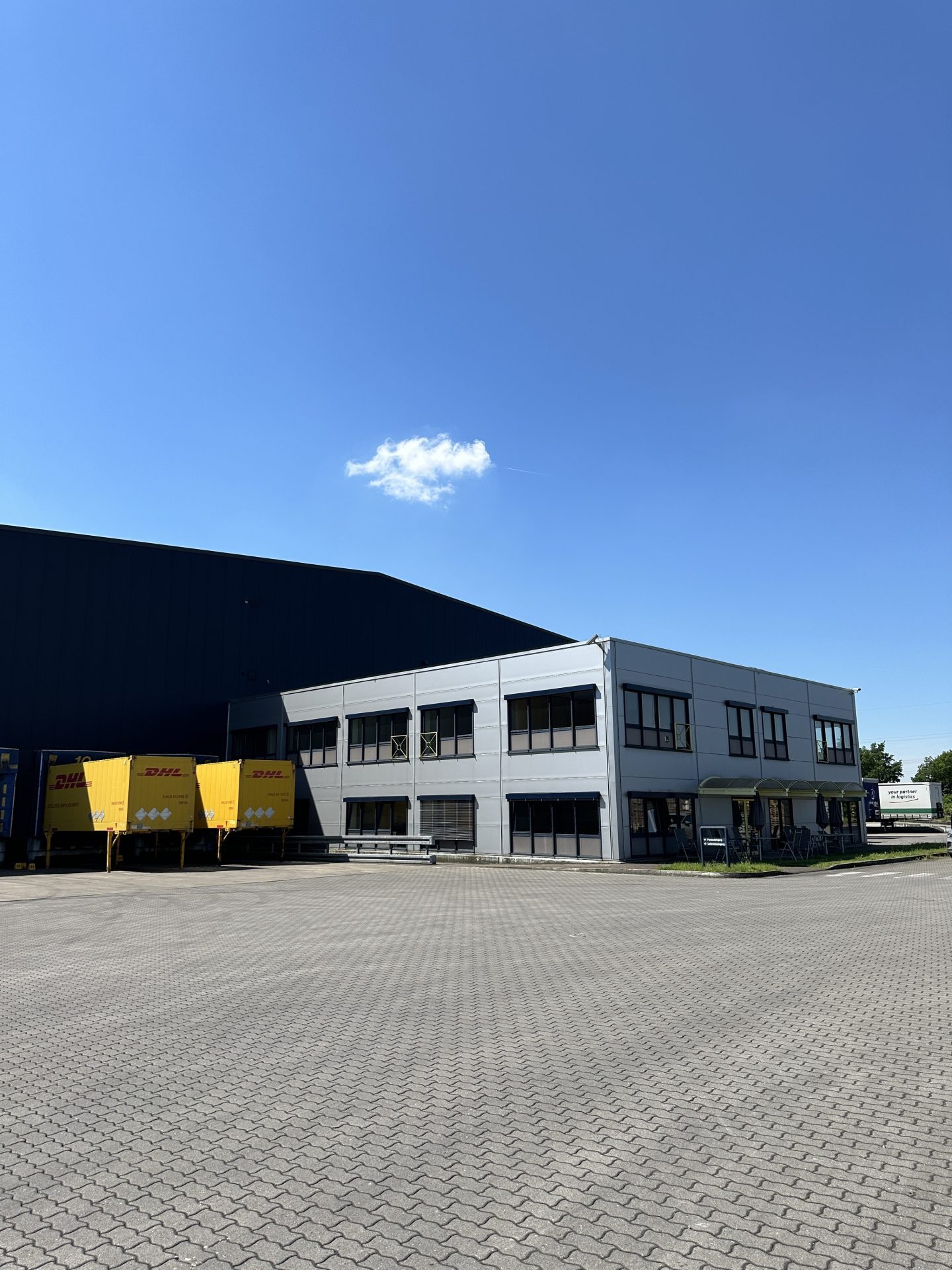 Office wing and loading ramps at the Hünxe site, with yellow DHL swap bodies at the doors