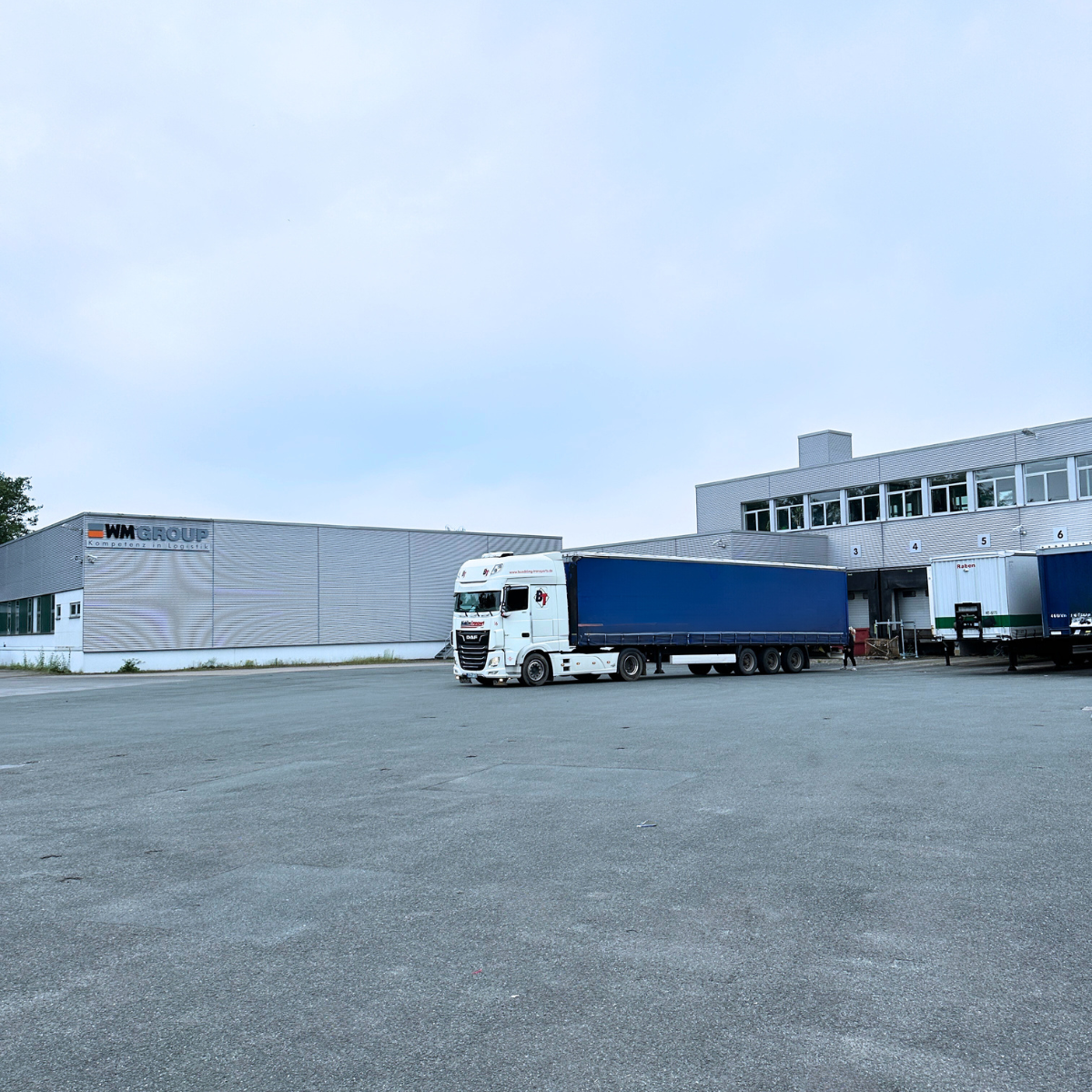 Articulated truck in the yard of a WM GROUP hall with several loading docks in use