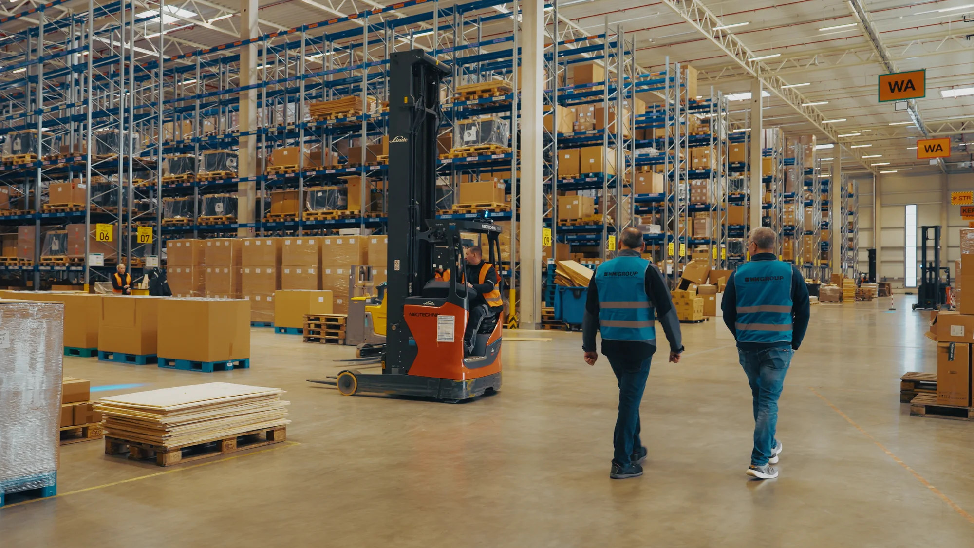 Two WM GROUP employees in the high-bay warehouse with a reach truck
