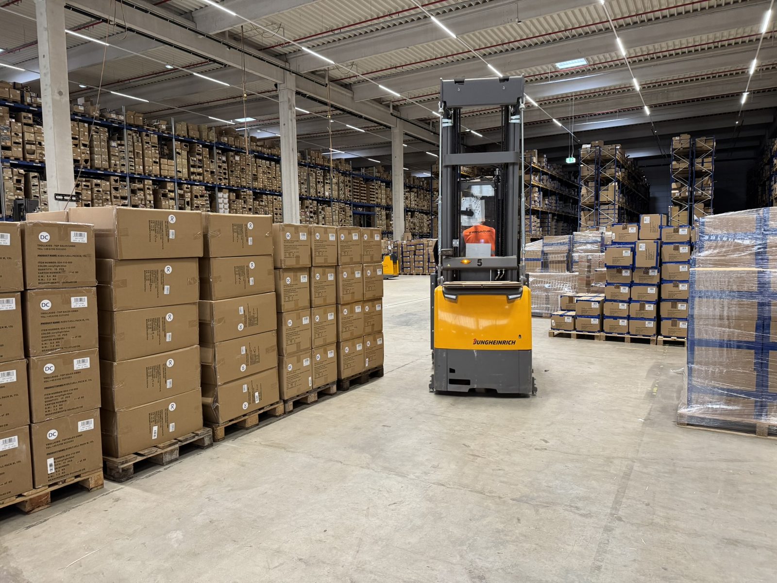 A warehouse aisle with an order picker and palletised shipping cartons.