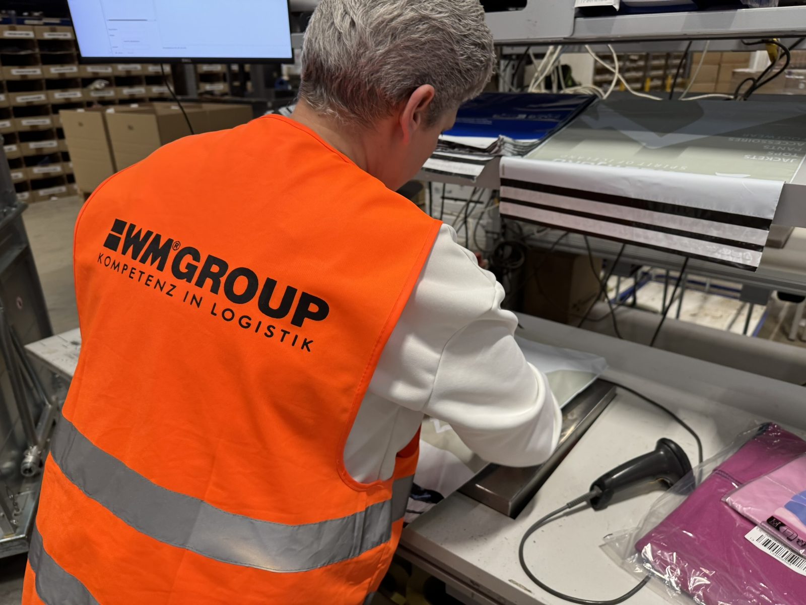 An employee in a WM GROUP hi-vis vest closing a shipment at the packing machine.